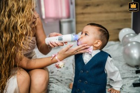 In Plovdiv, Bulgaria, the bride, holding a bottle, shares a tender moment of care with her toddler during a quiet pause on the wedding morning.